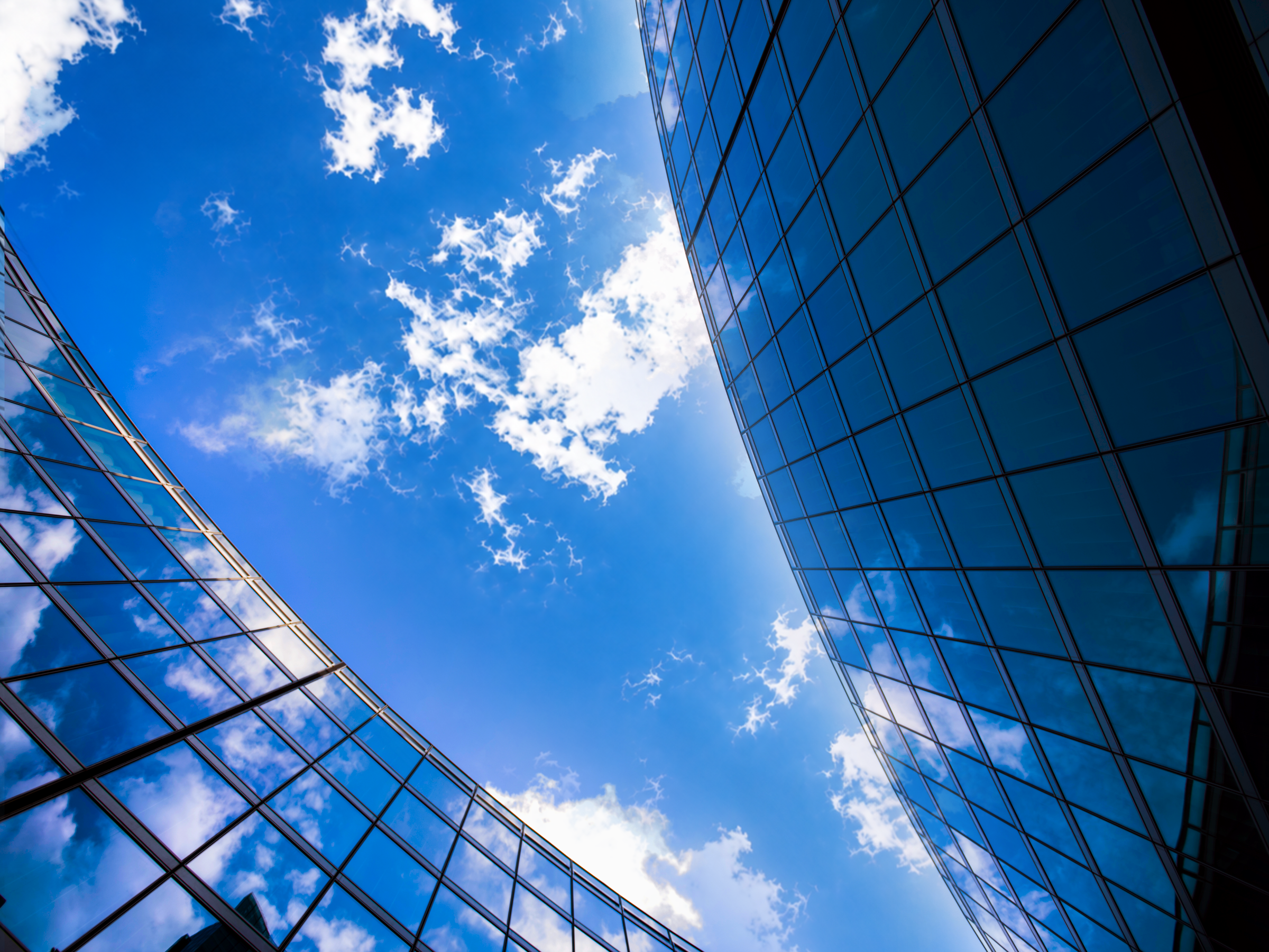 Two blue glass facades framing a wide open sky with white clouds, viewed from below